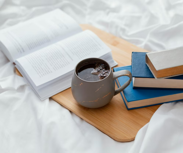Stack of books and a cup of coffee on a bed